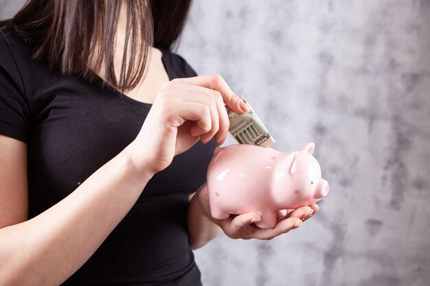 The girl puts a banknote in the piggy bank