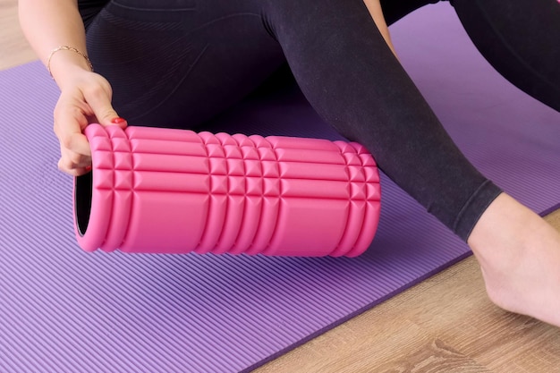 The girl puts a foam roller under her leg for a fitness massage Legs close up Pregnant yoga practice concept