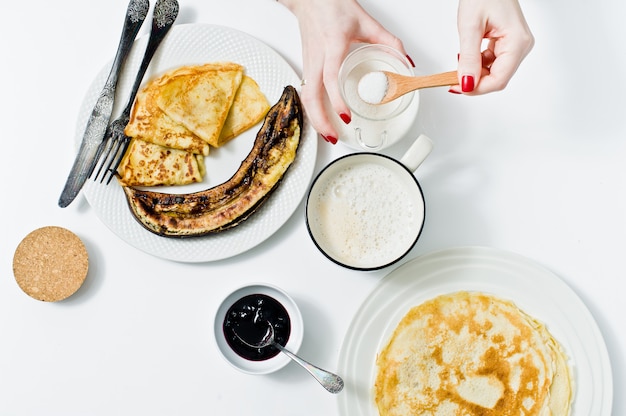 The girl puts a spoonful of cane sugar in a Cup of coffee, Breakfast with pancakes. 