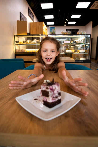 The girl reaches out with her hands for a sweet cake. Child in a cafe eats cake