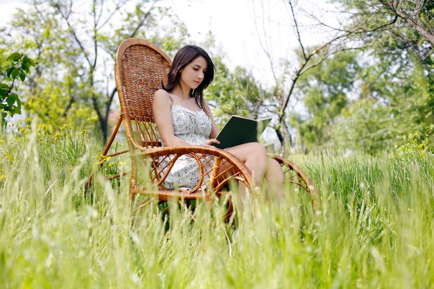 Girl read book in wicker rocking chair in grass