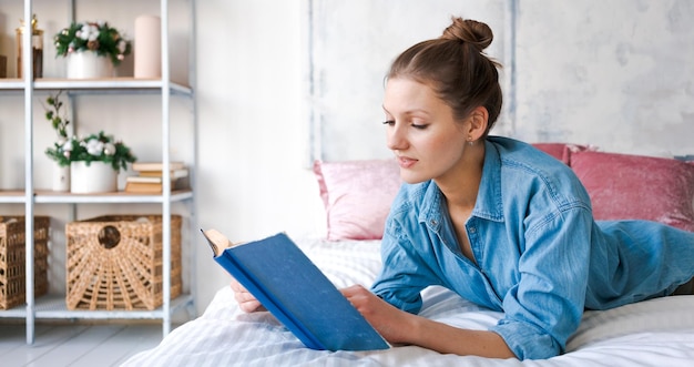 Girl reading book in bed lying on her stomach smiling happy and relaxed