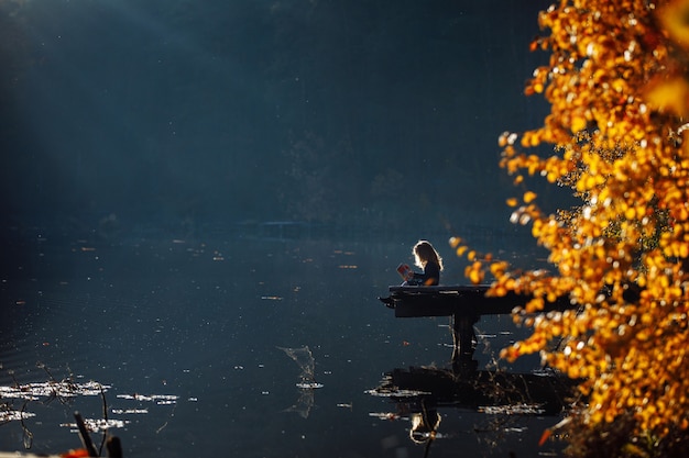 Girl reads a book in autumn by the river.