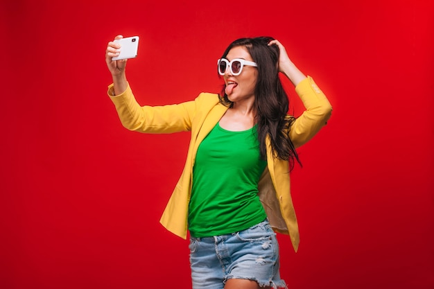 Girl on a red background in jacket takes a selfie on the phone