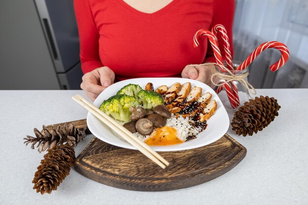 A girl in a red blouse and brown apron holds a plate of golden rice chicken broccoli shiitake mushrooms and unagi sauce in her hands The dish is decorated with sesame seeds Asian food concept