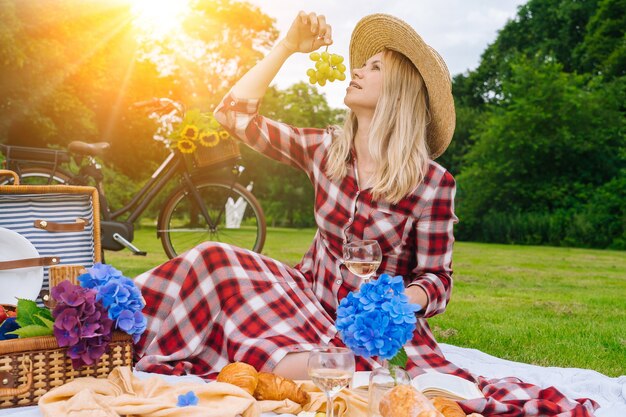 Girl in red checkered dress and hat sitting on white knit picnic blanket