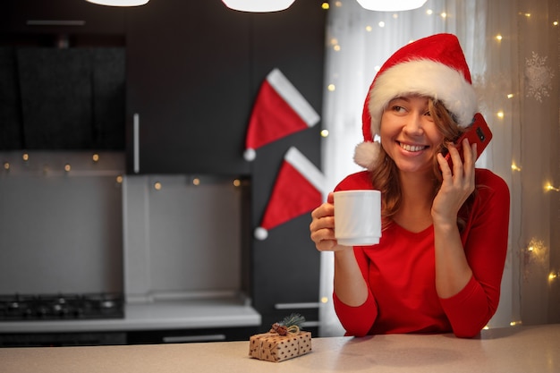 Girl in red clothes in the kitchen talking on a smartphone on christmas eve