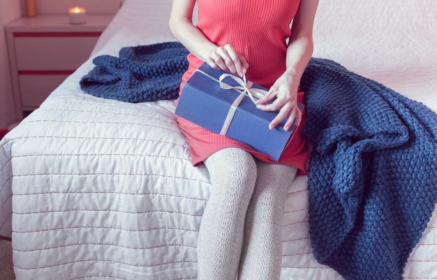 Girl in a red dress opens a gift while sitting on the bed