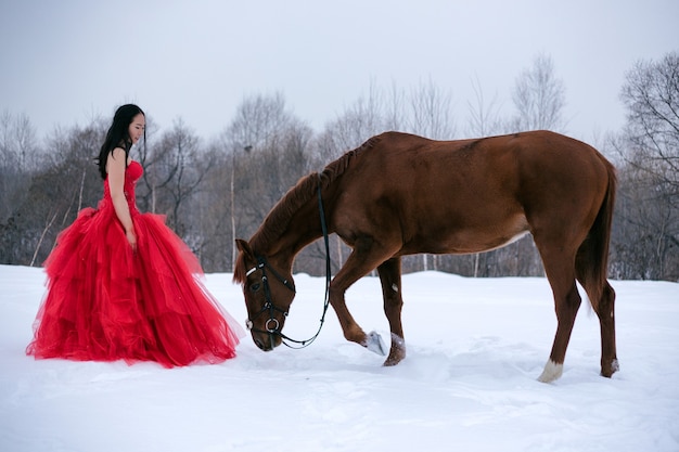 Girl in a red dress, with a horse, winter, brunette