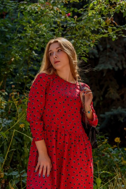 A girl in a red dress with long hair on a background of greenery in summer. beautiful girl in nature