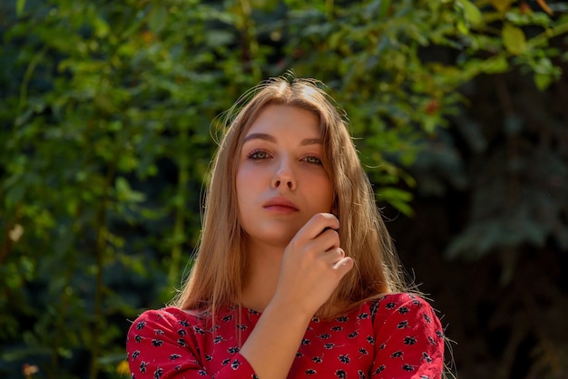 A girl in a red dress with long hair on a background of greenery in summer. beautiful girl in nature