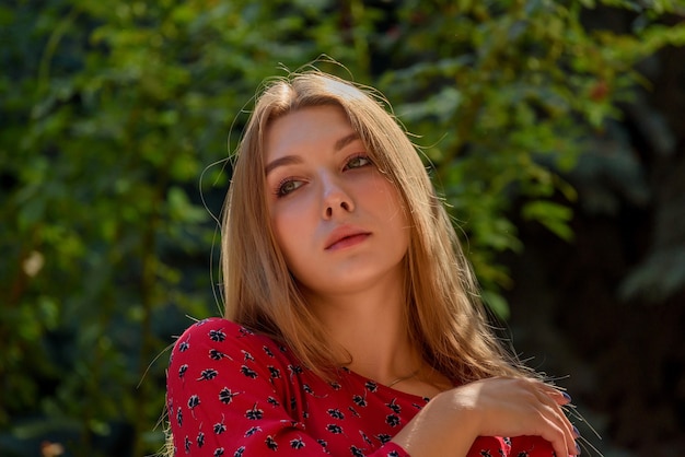 A girl in a red dress with long hair on a background of greenery in summer. beautiful girl in nature