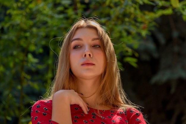 A girl in a red dress with long hair on a background of greenery in summer. beautiful girl in nature