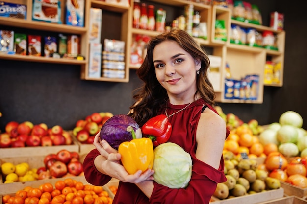 Girl in red holding different vegetables on fruits store