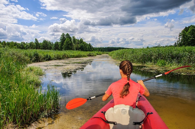 A girl on a red kayak paddles along the river in springUkraine