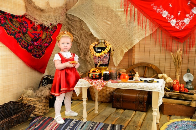 A girl in a red national costume near a table with a samovar and steering wheels Pancake day