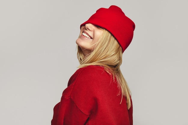 Girl in red outfit covers eyes with hat smiling broadly on white background