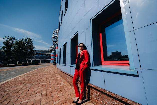 A girl in a red suit stands against the background of a modern building in the city