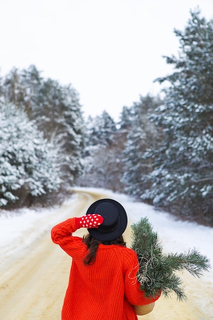 A girl in a red sweater and hat stands in the middle of a snowy road in a forest with pine branches Weekend trip