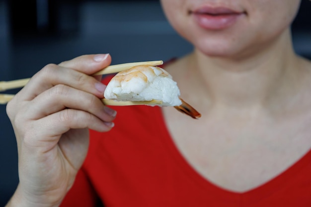 A girl in a red sweater holds sushi with king prawns with chopsticks Seafood