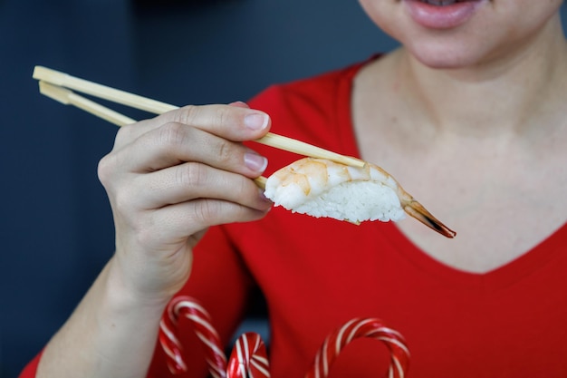 A girl in a red sweater holds sushi with king prawns with chopsticks Seafood