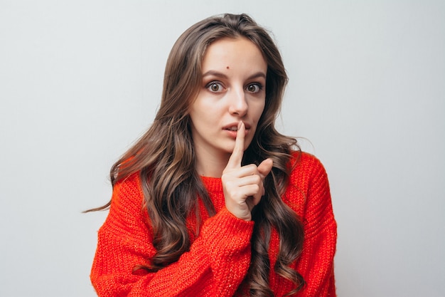 Girl in a red sweater shows her finger silence.