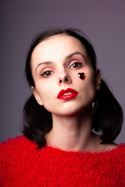 girl in a red sweater with red lips and a red heart on her forehead portrait