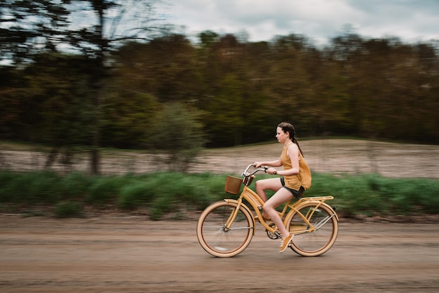 Girl riding her yellow bike on a dirt road in the summer