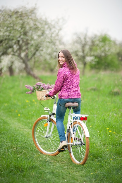 Girl riding a vintage white bicycle with lilac flowers basket in spring garden