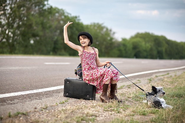 Girl on the road with old suitcase and dog stoped auto