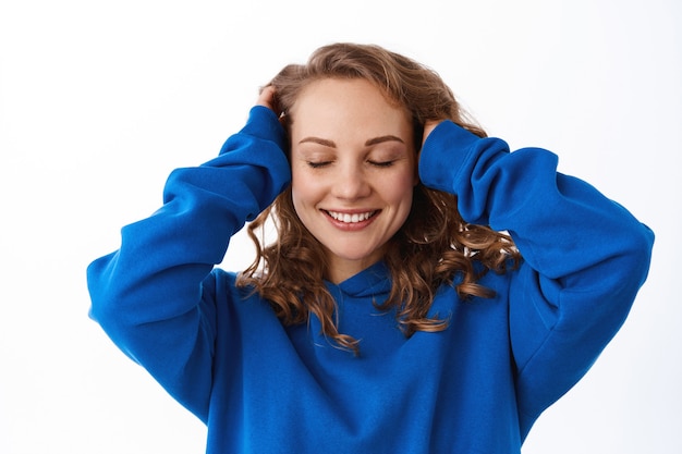 Girl run hand through hair and smiling delighted, pleased with new hairdo, feel softness of hair after shampoo, standing pleased against white wall