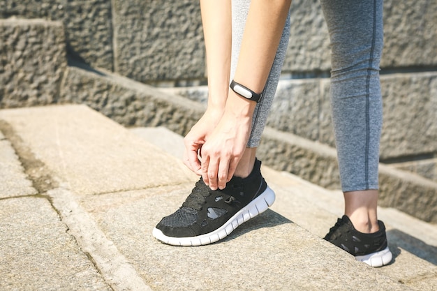 Girl runner tying laces for jogging her shoes on road in a park