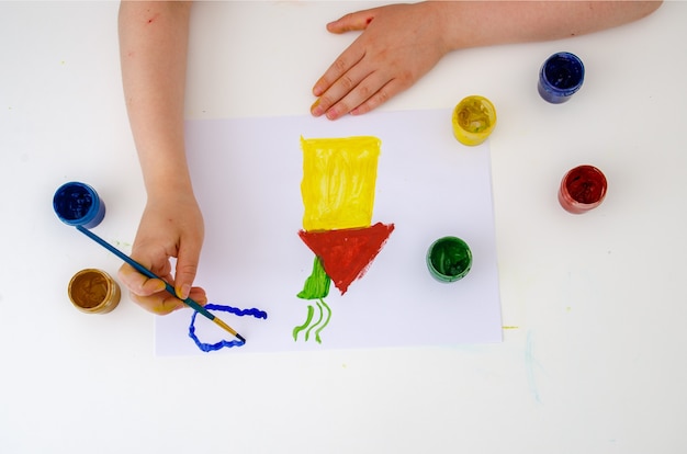 The girl's hand draws a house with colored paints on drawing paper