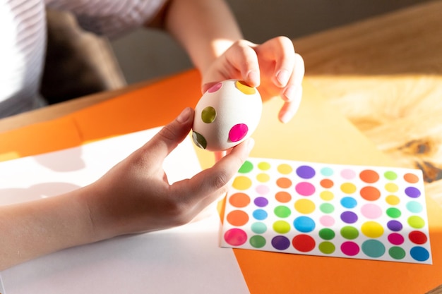 A girl's hand paints an Easter egg with a yellow brush closeup The concept of the holiday and Easter decorChildish art handmade culture conceptCaucasian girl paints eggsEaster holiday