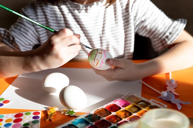 A girl's hand paints an Easter egg with a yellow brush closeup The concept of the holiday and Easter decorChildish art handmade culture conceptCaucasian girl paints eggsEaster holiday