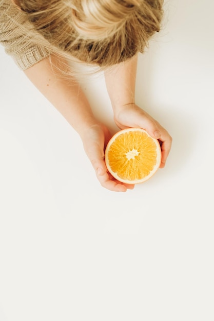 Girl's hands holding half of cutted orange on white background Top view flat lay