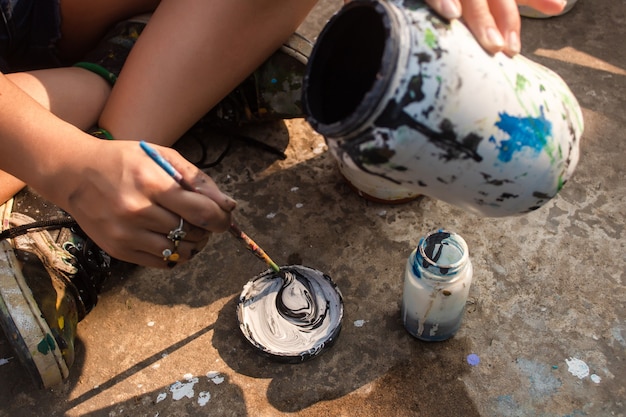 Girl's hands mixing black and white paint on a lid in the street.