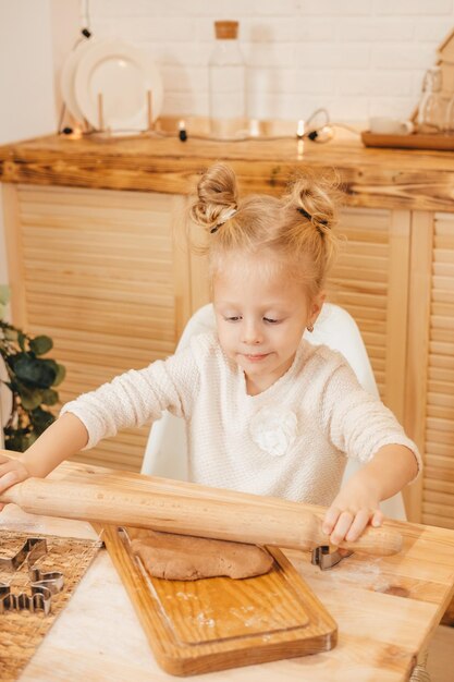 Girl's hands rolls out ginger dough with a rolling pin in the kitchen Girl preparing christmas cookies on a wooden table