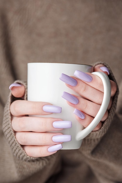 Girl's hands with delicate purple manicure holding a cup of tea