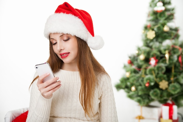 Girl in santa hat call phone by christmas tree