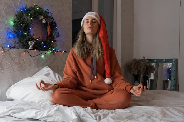 A girl in a Santa hat meditates on the bed. Happy New Year 2022