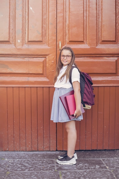 Girl in school uniform with backpack before big doors