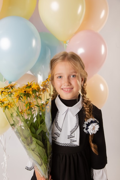 Girl schoolgirl, first grade student in school uniform on a white background with balls and flowers