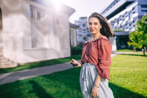 Girl schoolgirl holding a phone in her hands looking at the camera in the open air