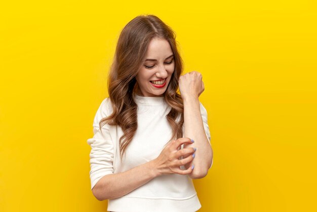 Photo girl scratches her hand on yellow isolated background woman suffers from psoriasis