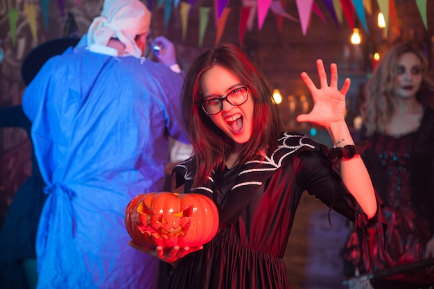 Photo girl screaming to the camera dressed up like a witch with a pumpking celebrating halloween with her friends.