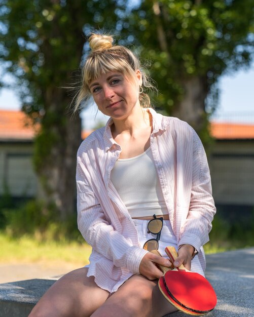 a girl in short shorts sits on a tennis table and holds two tennis rackets in her hands