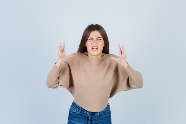 girl showing claws imitating a cat in aggressive manner in sweater, jeans and looking irritated.