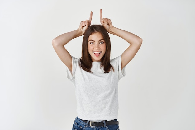 Girl showing inner devil Portrait of charming cute and confident european female with tattoo on arm holding index fingers like demon horns on head and smiling with intrigued delighted face