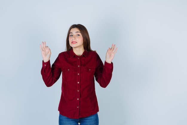 Girl showing ok gesture in burgundy blouse and looking careful